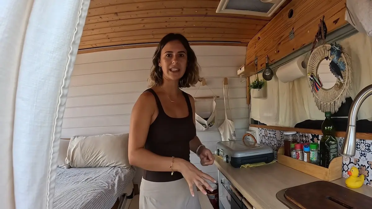 Sara muestra el área de cocina equipada con hornalla y fregadero en la camper