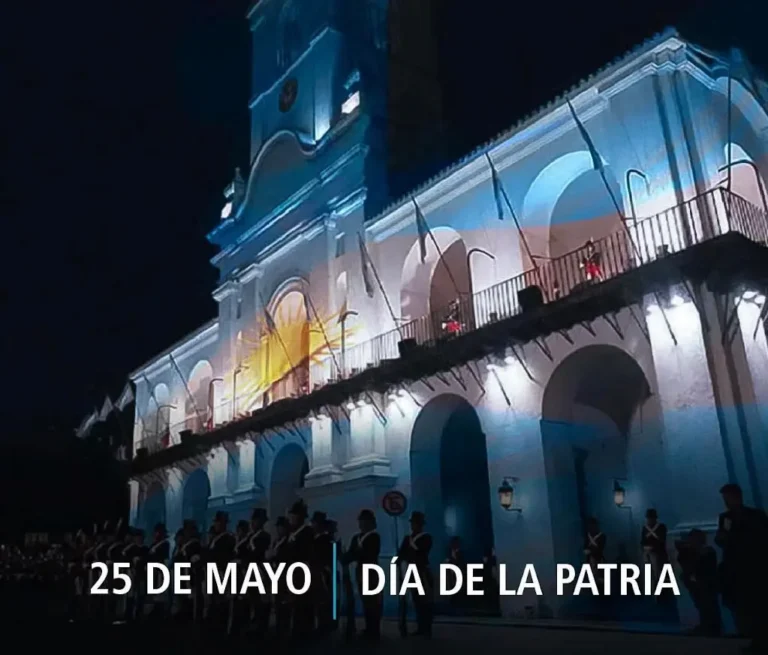 Recreación histórica del Cabildo de Buenos Aires en mayo de 1810, con su fachada blanca completa y cúpula central, y una multitud de ciudadanos con vestimenta colonial celebrando en la plaza bajo la lluvia.