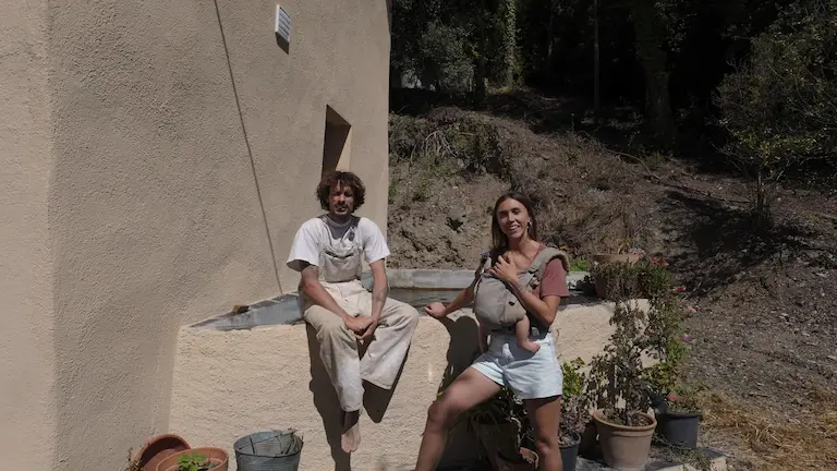 Alex y Paola con su bebé junto al depósito de agua de río en su masía autosuficiente en el Montseny.