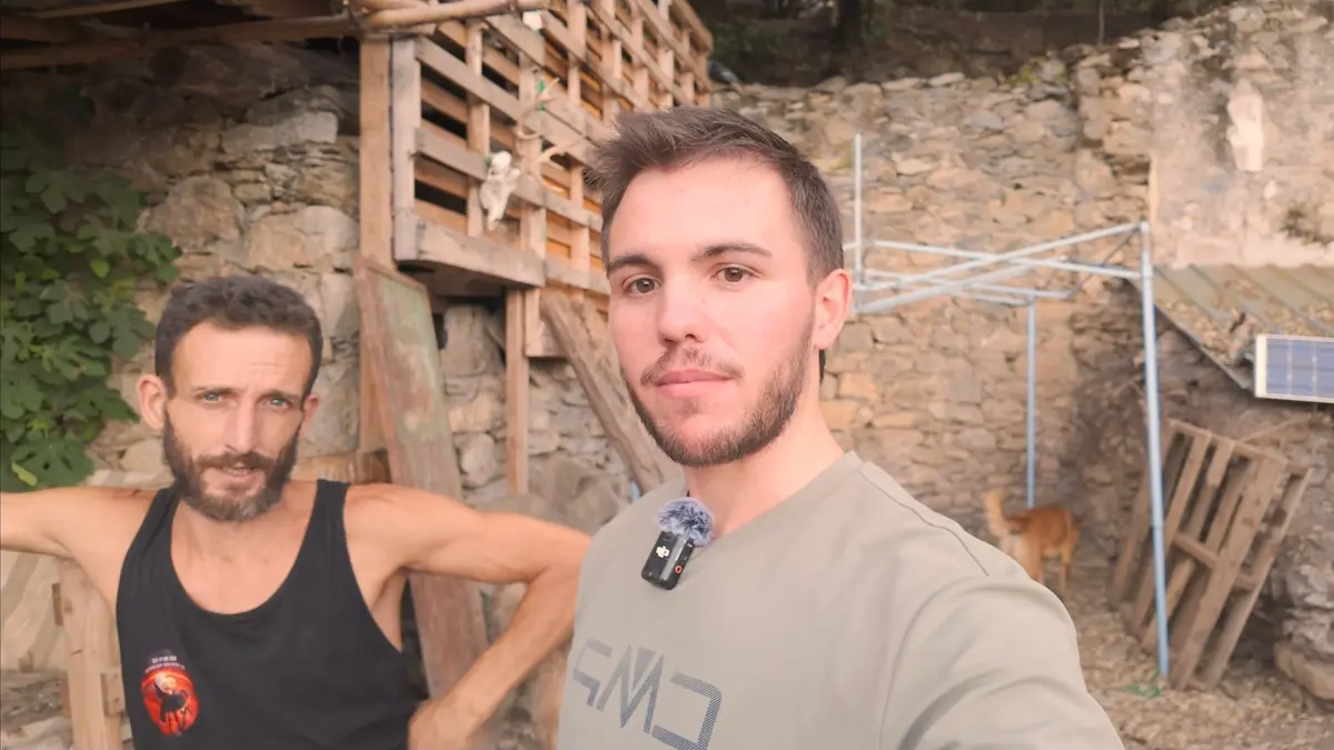 Arnau Serrado junto a Bernat frente a la estructura construida con materiales reciclados y muros de piedra en la montaña.