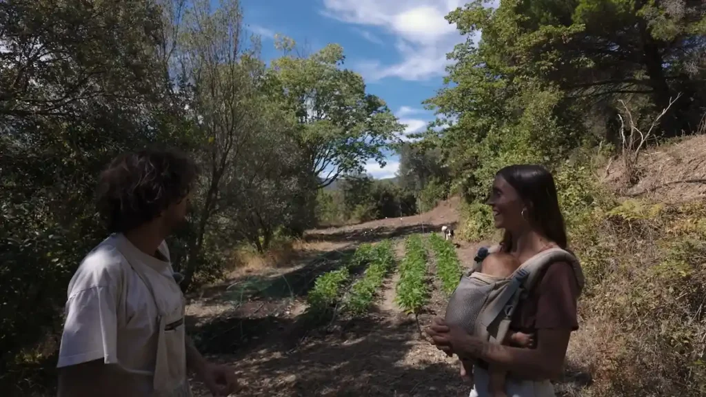 Alex y Paola con su bebé recorriendo los bancales de hortalizas en el huerto orgánico de Can Dansa.
