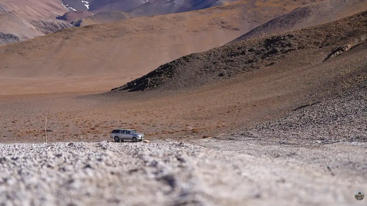 Camioneta 4x4 de color gris avanzando por un terreno de piedras blancas y suelo desértico, rodeada por la inmensidad del paisaje montañoso y árido de la Puna en Catamarca.