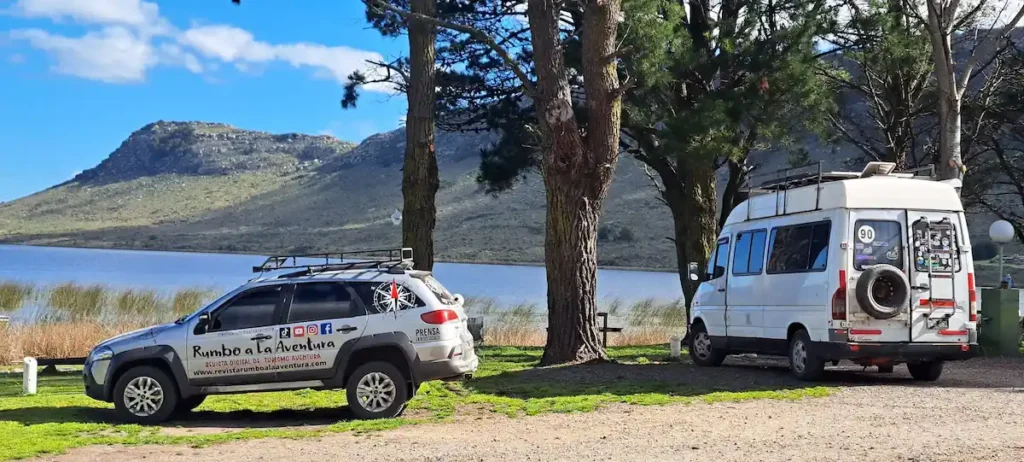 Vehículo de Rumbo a la Aventura y motorhome estacionados en la costa frente a las sierras en el Club de Pesca Balcarce de Laguna La Brava