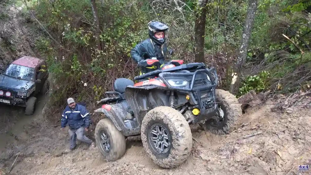 Piloto con casco sobre cuatriciclo ATV en ascenso embarrado en Chile con otra camioneta y persona de fondo.