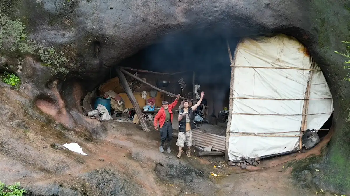 Vista abierta de Don Pedro y Sergio saludando con los brazos en alto junto a la entrada del refugio de roca en Tucumán