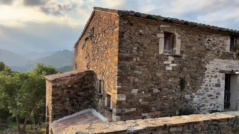 Fachada de piedra y tejado de tejas de la masía de 300 años con las montañas del Pirineo al fondo.