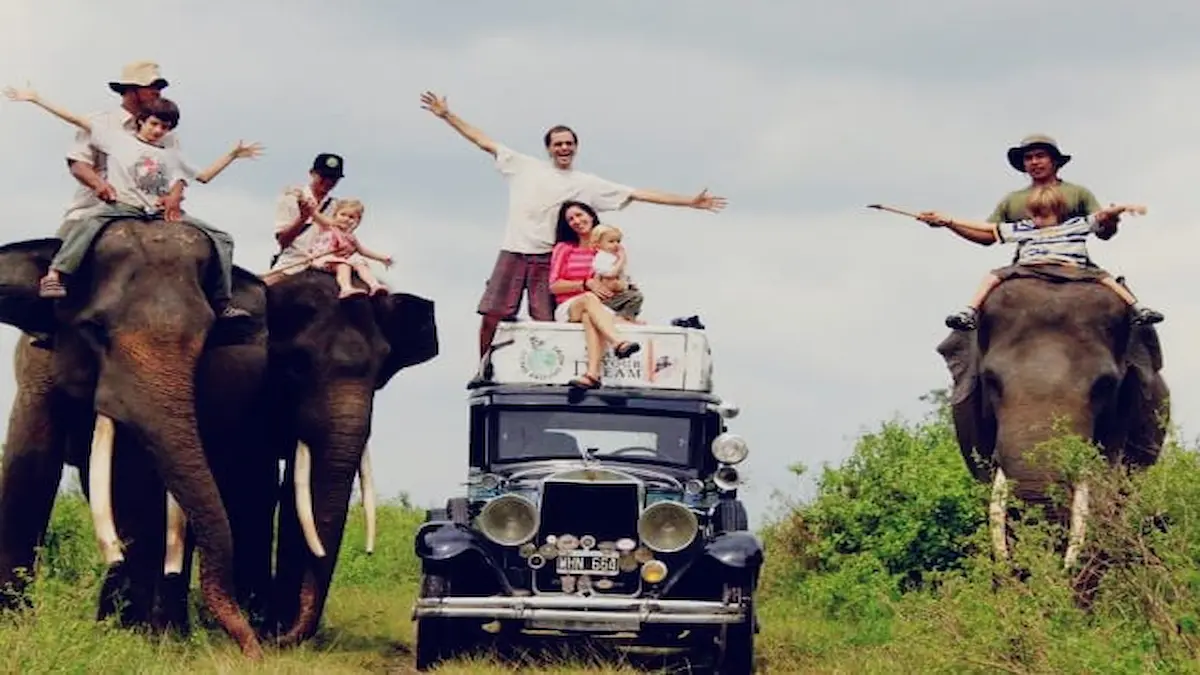 Una fotografía colorida de la familia Zapp al completo (padre, madre y cuatro hijos) posando alegremente sobre su auto clásico Graham-Paige de 1928, apodado "Macondo", y sobre tres elefantes asiáticos en un entorno de selva verde bajo un cielo nublado, durante su viaje por Asia.