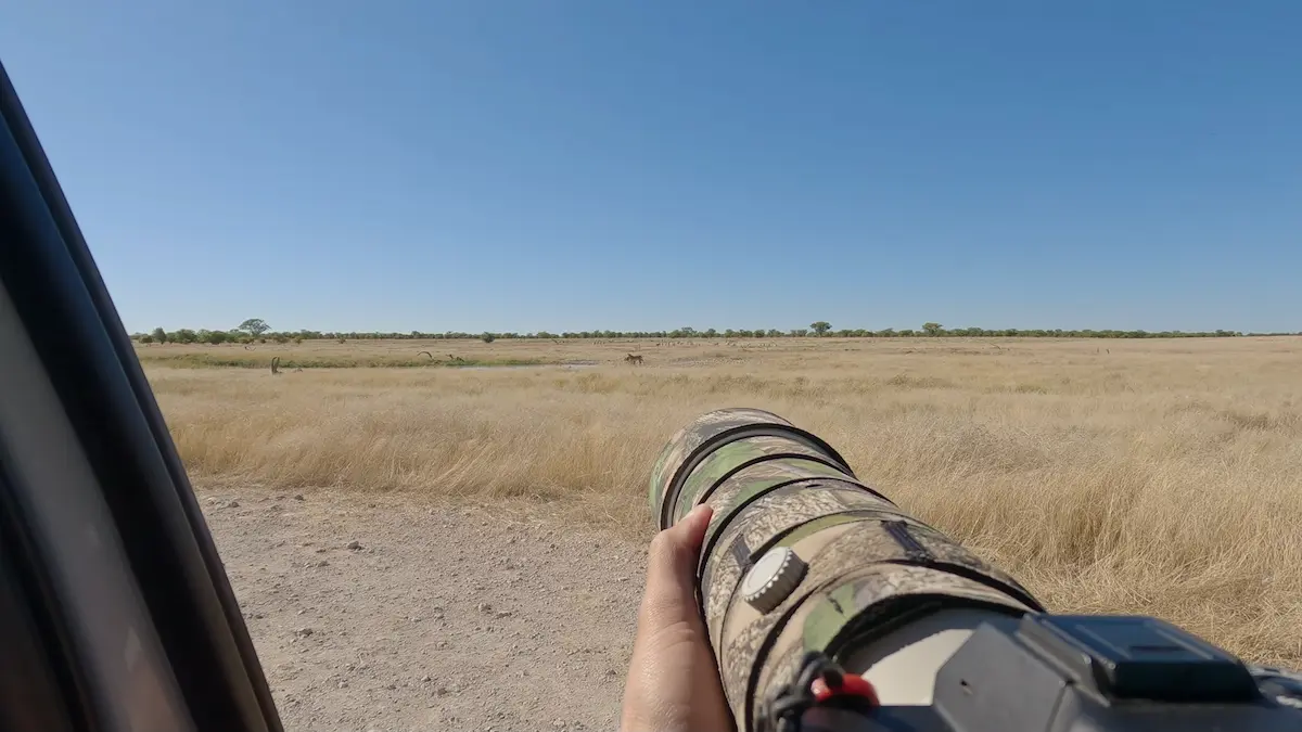 Primer plano de una lente de cámara con camuflaje apuntando hacia la savana en el Parque Nacional Etosha, Namibia.
