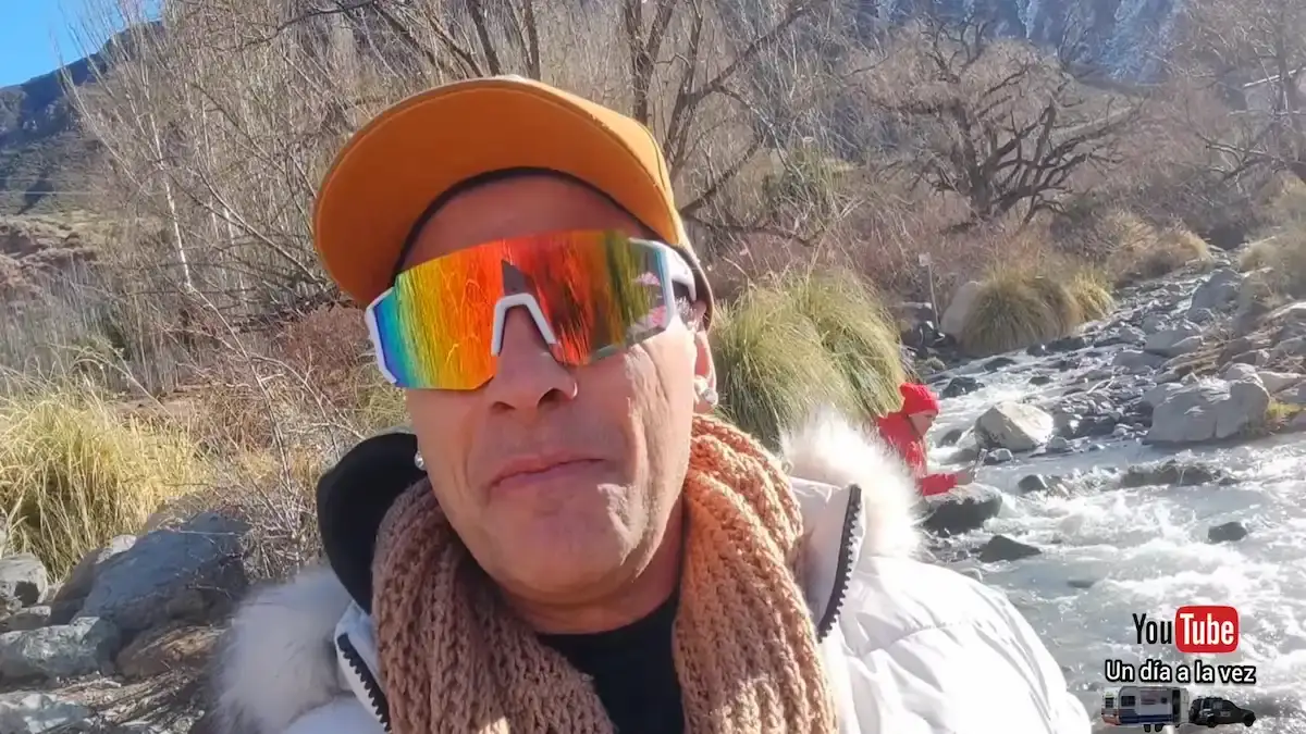 Javier y Fátima, embajadores de la Red Rumbo, caminan junto a un arroyo que corre entre piedras y orillas nevadas en un valle de alta montaña.