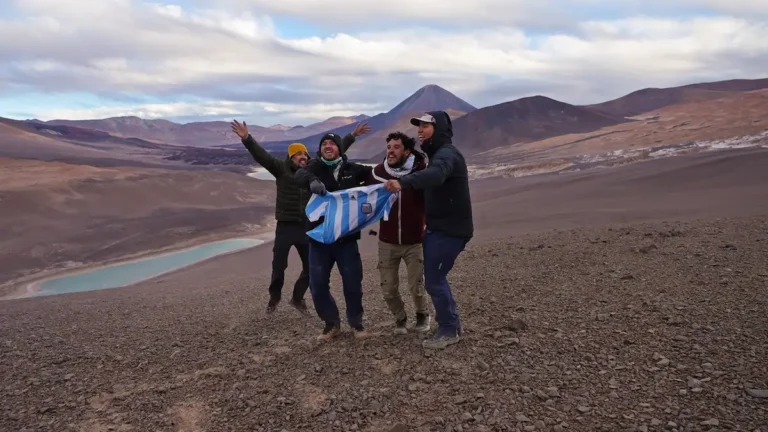 Lean Gon y sus compañeros festejan saltando y sosteniendo la camiseta de la Selección Argentina en un paisaje montañoso y árido al pie del Volcán Peinado en Catamarca.
