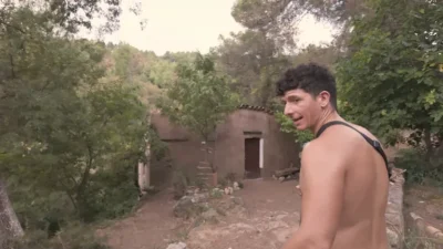 Mark de espaldas señalando la antigua barraca de piedra restaurada rodeada de vegetación en una finca de Cataluña.