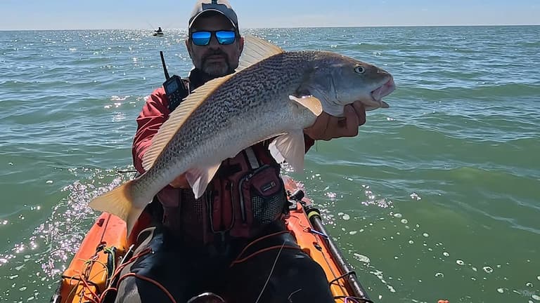 Pescador exhibiendo una gran corvina rubia capturada en kayak en Santa Teresita