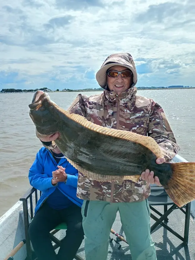 Pescador sosteniendo con ambas manos un lenguado gigante a bordo de una embarcación en la albufera de Mar Chiquita.