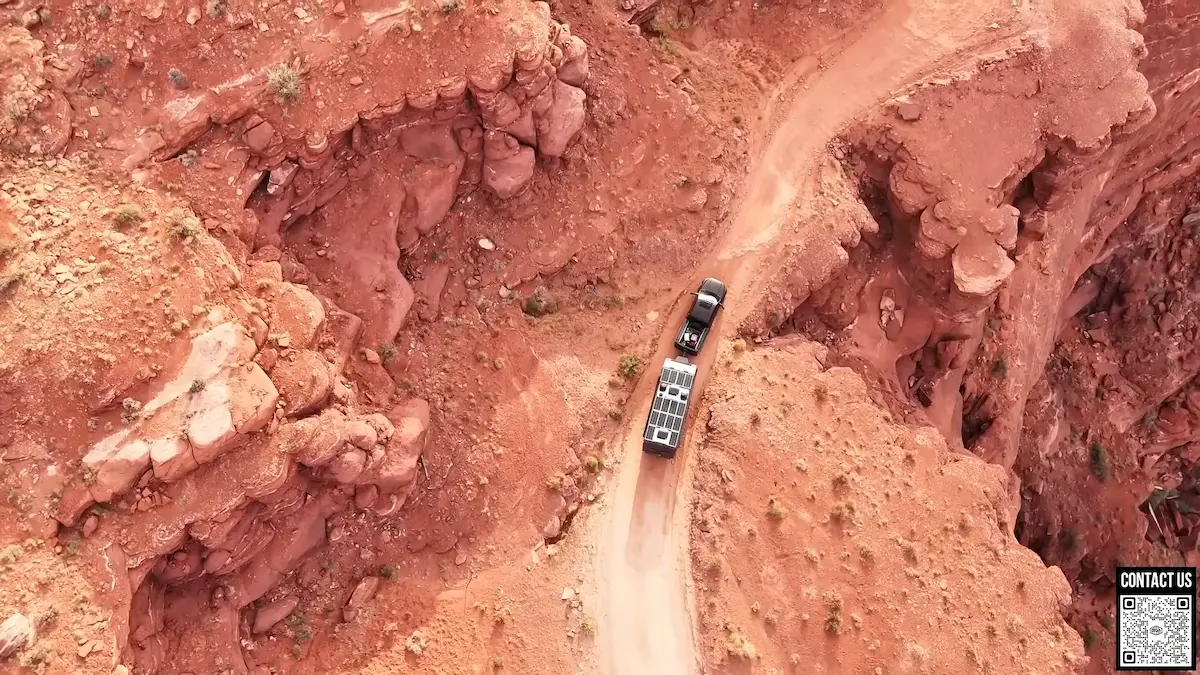 Vista aérea de un remolque de aventura Roamer X con paneles solares en el techo, transitando por un camino estrecho entre cañones de roca roja.