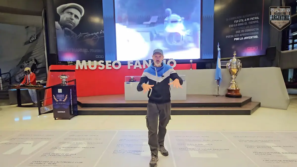 Presentador de Rodando por Argentina en el hall principal del Museo Fangio frente a trofeos, pantallas y homenajes a Juan Manuel Fangio.