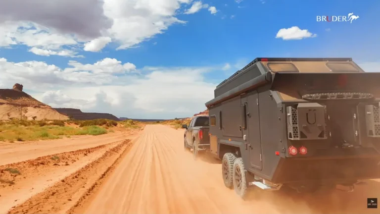 Casa rodante de tiro extrema Bruder EXP-10 siendo remolcada por una camioneta negra en un camino de arena roja en el desierto.