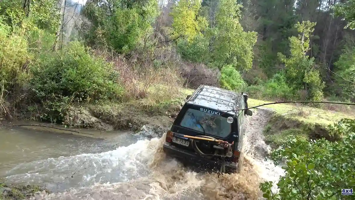 Camioneta Suzuki 4x4 cruzando un río caudaloso en un entorno de bosque en Chile.