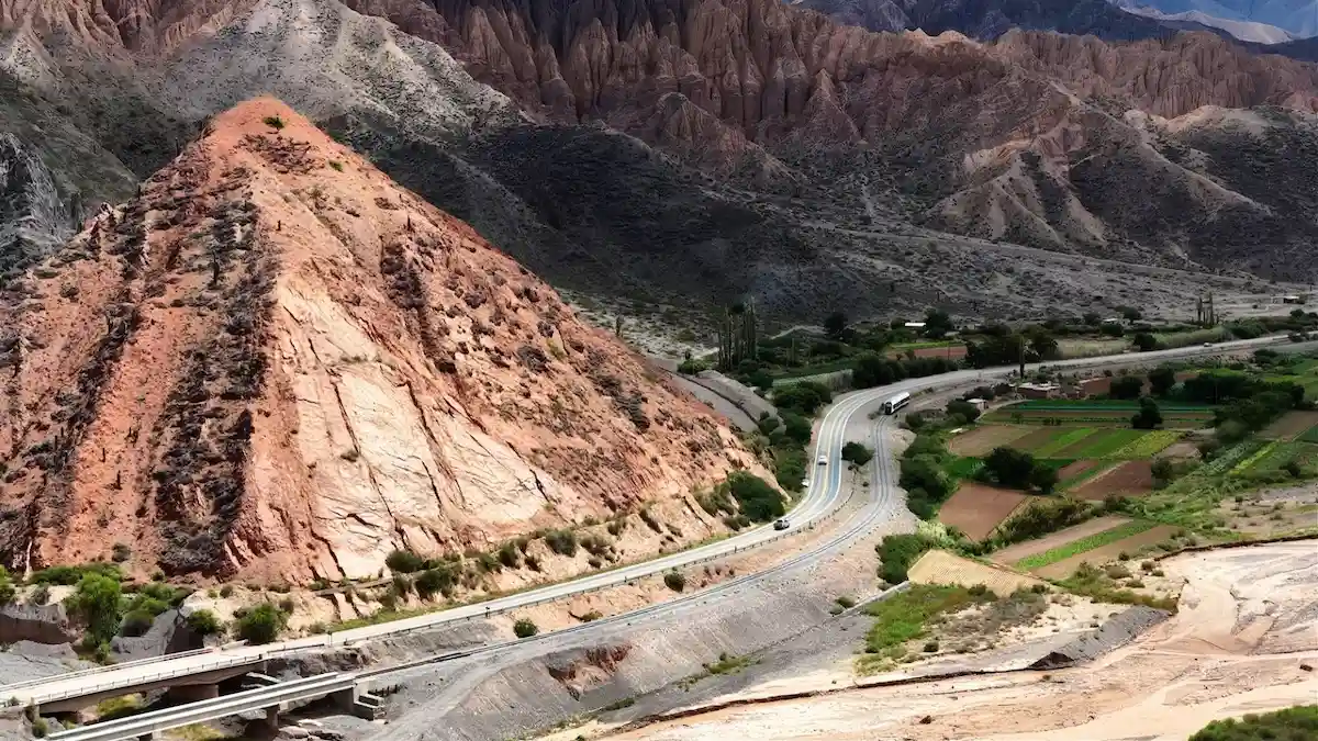 El Tren Solar de la Quebrada transitando por una curva de montaña sobre murallones de piedra, con el paisaje de cerros coloridos de fondo.