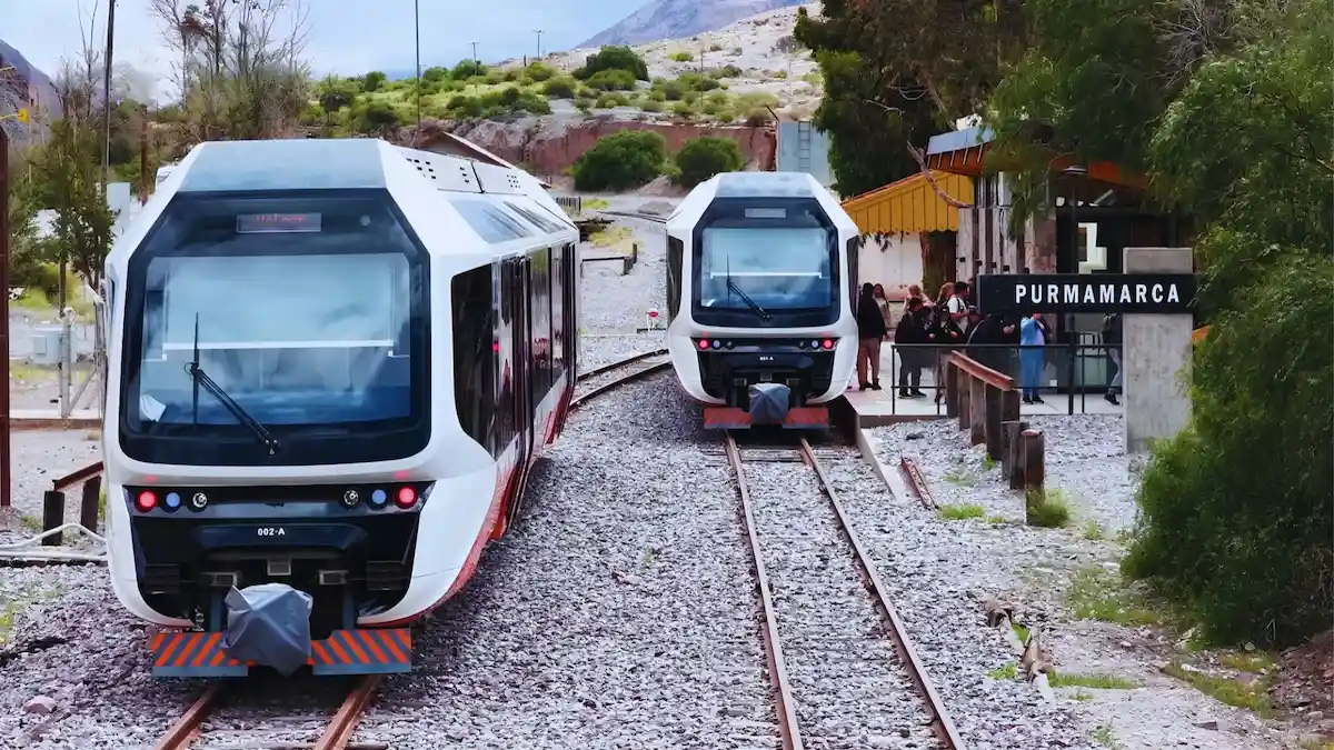 El moderno Tren Solar de la Quebrada detenido en la estación de Purmamarca, con los cerros coloridos de Jujuy de fondo bajo un cielo azul